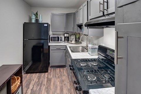 A kitchen with a black fridge and a black stove top.