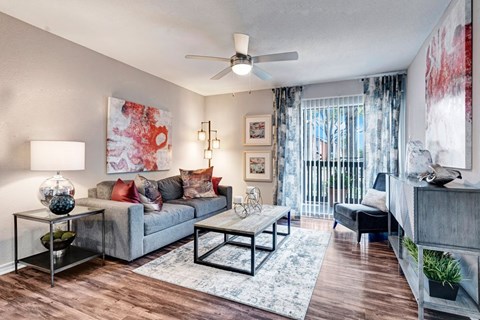 A living room with a grey couch, a glass table, and a ceiling fan.