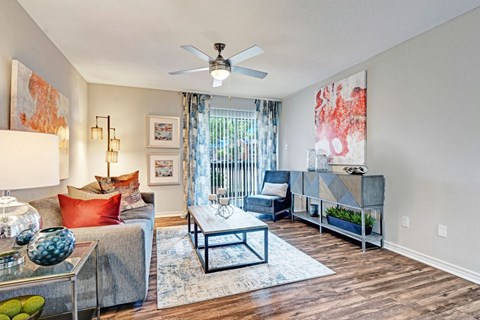 A living room with a grey couch, a glass coffee table, and a ceiling fan.