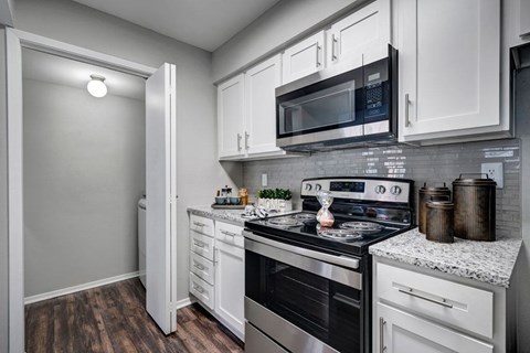 A kitchen with a black microwave above a stove and white cabinets.