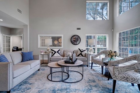 A living room with a grey couch, a round table, and a clock on the wall.