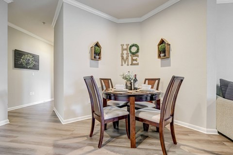 A dining room with a table set for two and a "HOME ME" sign on the wall.