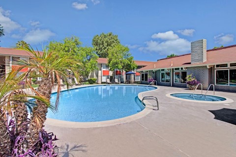 A pool surrounded by a concrete patio and a building in the background.