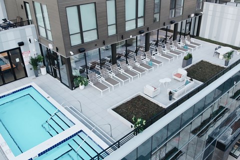 A rooftop pool area with sun loungers and a glass railing.