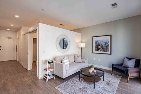 A living room with a white couch, a round mirror, and a coffee table.