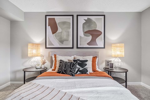 A bedroom with a bed, two lamps, and two framed artworks on the wall.