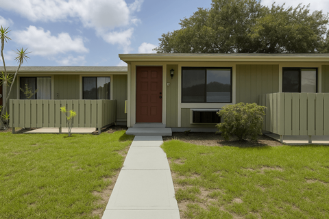 A small house with a red door and a concrete walkway in front.