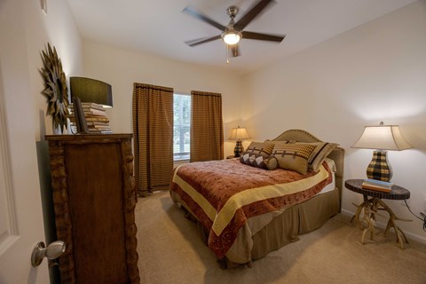 A bedroom with a bed, a dresser, and a ceiling fan.