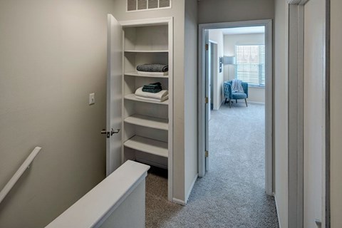 A white bathroom with a white tub and a white closet with shelves.