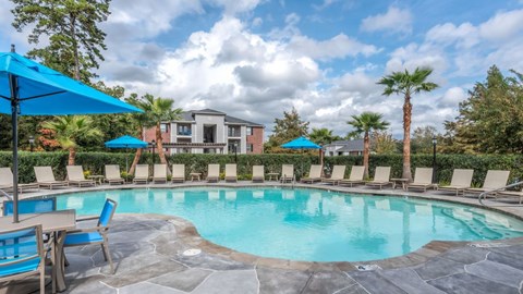 A swimming pool surrounded by lounge chairs and umbrellas with a building in the background.