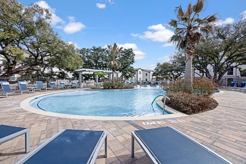 A pool surrounded by trees and chairs.