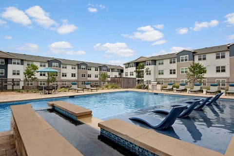 A swimming pool with a bench and apartment buildings in the background.