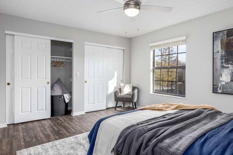 A bedroom with a bed, chair, and a window.