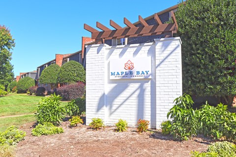 A white building with a sign that says "Maple Bay" in front of a grassy area.