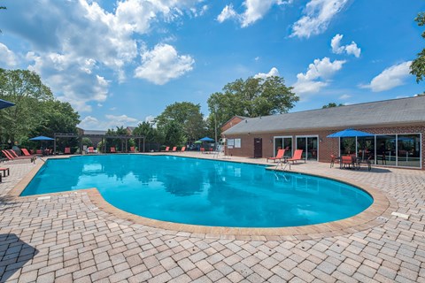 A large outdoor swimming pool surrounded by a brick patio and lounge chairs.
