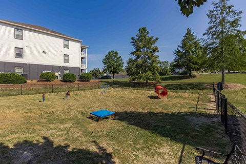 A playground with a blue mat and red slide is in front of a white apartment building.