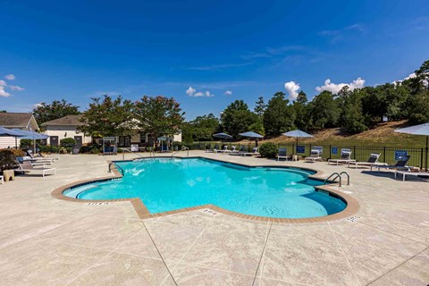 A large outdoor swimming pool surrounded by a concrete patio and lounge chairs.
