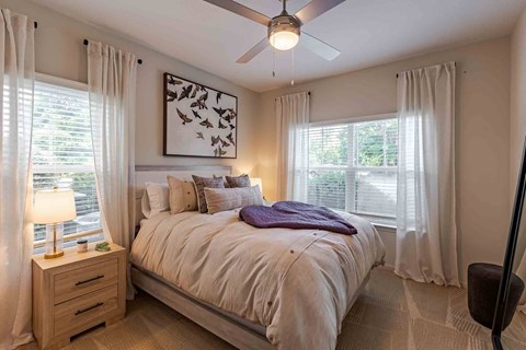 A bedroom with a bed, a ceiling fan, and a painting on the wall.