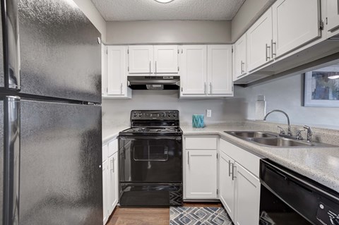 A black refrigerator is in a kitchen with white cabinets.