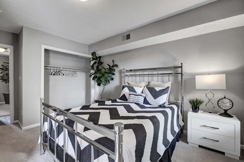 A bedroom with a bed, nightstand, and a plant.