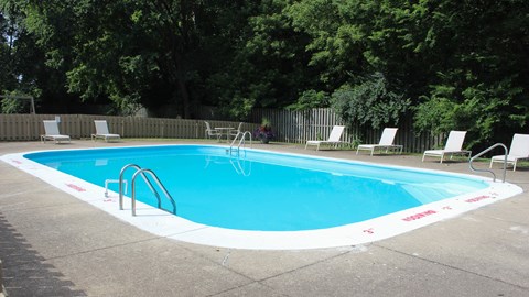 A small pool with a metal ladder and white chairs around it.