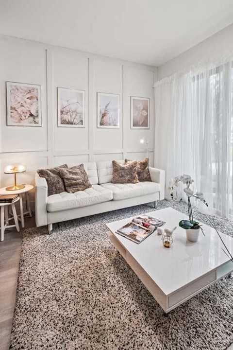 A white couch with brown pillows sits in a living room with a glass coffee table in front of it.