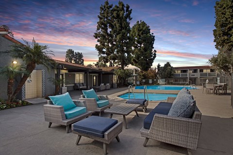A poolside area with wicker furniture and a tree.