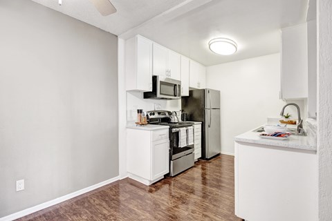 A kitchen with white cabinets and appliances, a wooden floor, and a ceiling fan.