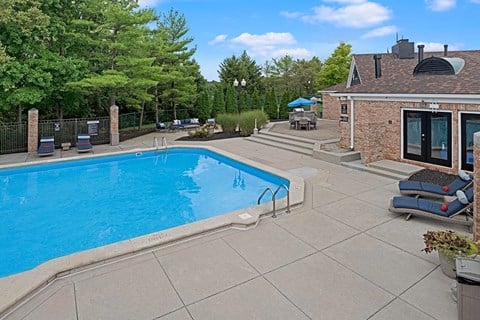 A swimming pool in a backyard with a house and trees in the background.