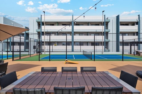 A table and chairs are set up on a patio with a pool and a building in the background.