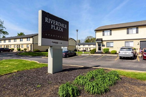A sign for Riverdale Plaza Apartments stands in front of the building.