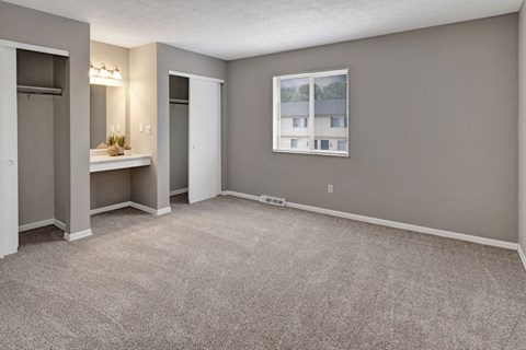 A room with grey carpet and a window showing a building outside.