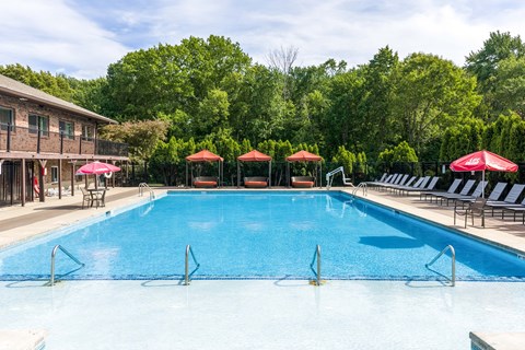 A large blue swimming pool surrounded by red umbrellas and lounge chairs.