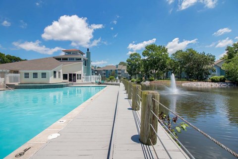 A wooden dock extends into a blue pool with a building in the background.