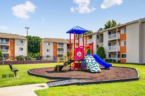 A playground with a blue umbrella and a red slide in front of apartment buildings.