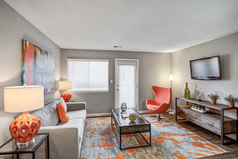 A living room with a grey couch, a red chair, a wooden coffee table, and a flat screen TV mounted on the wall.