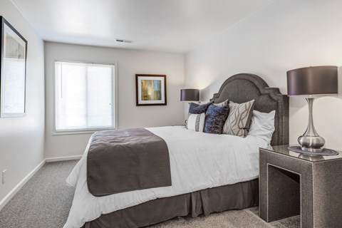 A bedroom with a large bed and a lamp on a side table.