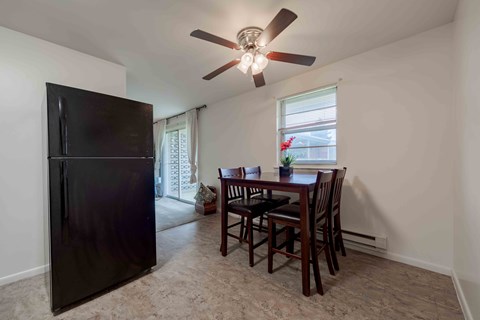 A black fridge sits in a kitchen with a table and chairs.