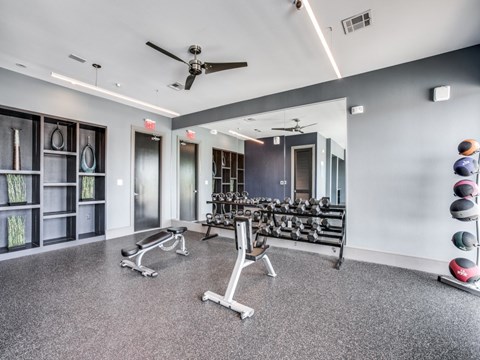 A spacious gym with a variety of equipment including dumbbells, weight plates, and a bench press.