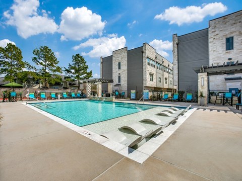 A large outdoor swimming pool with loungers and trees in the background.