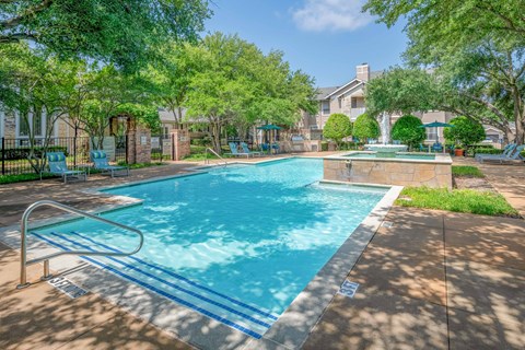 A swimming pool surrounded by trees and a fountain.