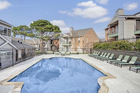 A swimming pool surrounded by lounge chairs and a fence.