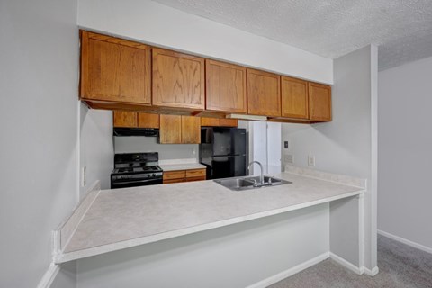 A kitchen area with a sink, stove, and oven under wooden cabinets.