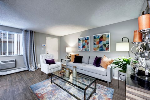 A living room with a white sofa, a glass coffee table, and a large window with curtains.
