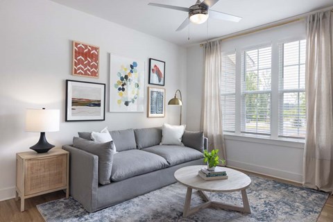 A living room with a grey couch, a side table with a lamp, a coffee table, and pictures on the wall.