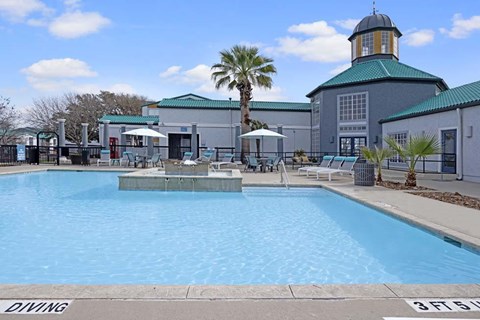 A large swimming pool with a diving board and a building with a green dome in the background.
