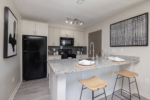 A kitchen with a black refrigerator, a granite countertop, and a bar stool.