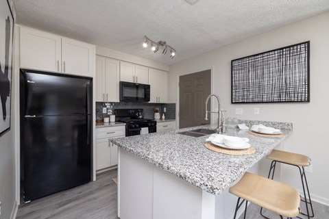 A kitchen with a black refrigerator and a granite countertop.