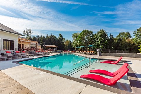 A pool with red chairs and a building in the background.