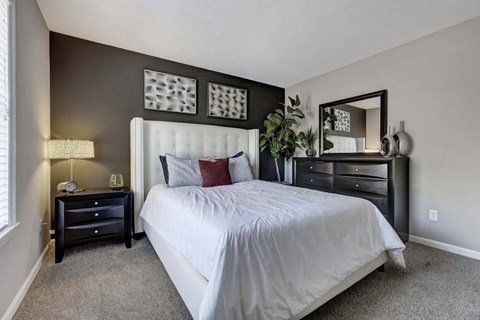 A bedroom with a large bed, a nightstand with a lamp, and a mirror above the dresser.